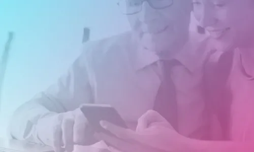 Image of an older man looking at a phone with a younger woman. There is a laptop open in front of them.