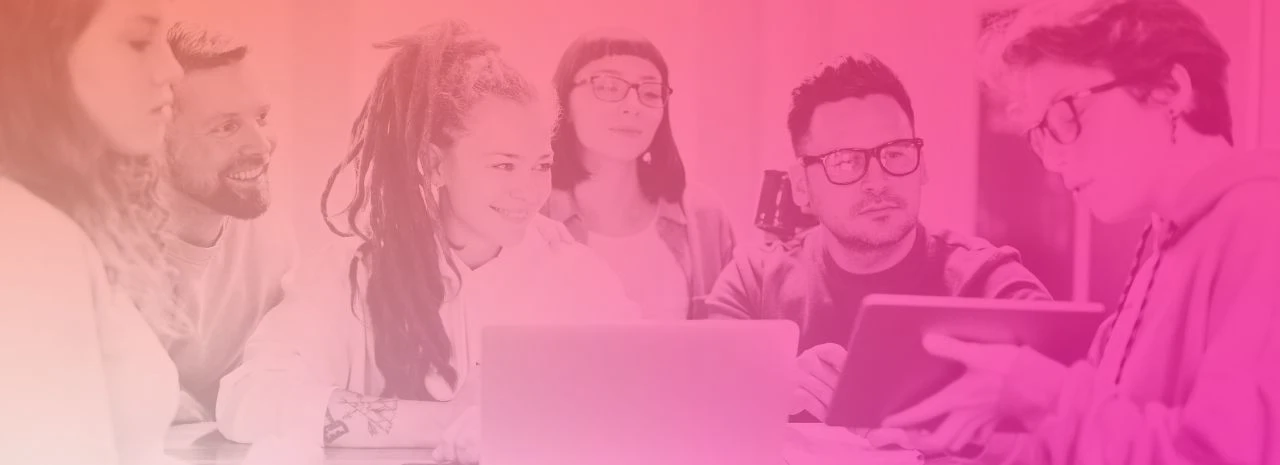 Image shows a group of people gathered around a desk. One person is holding an iPad and showing what's on it to the group.