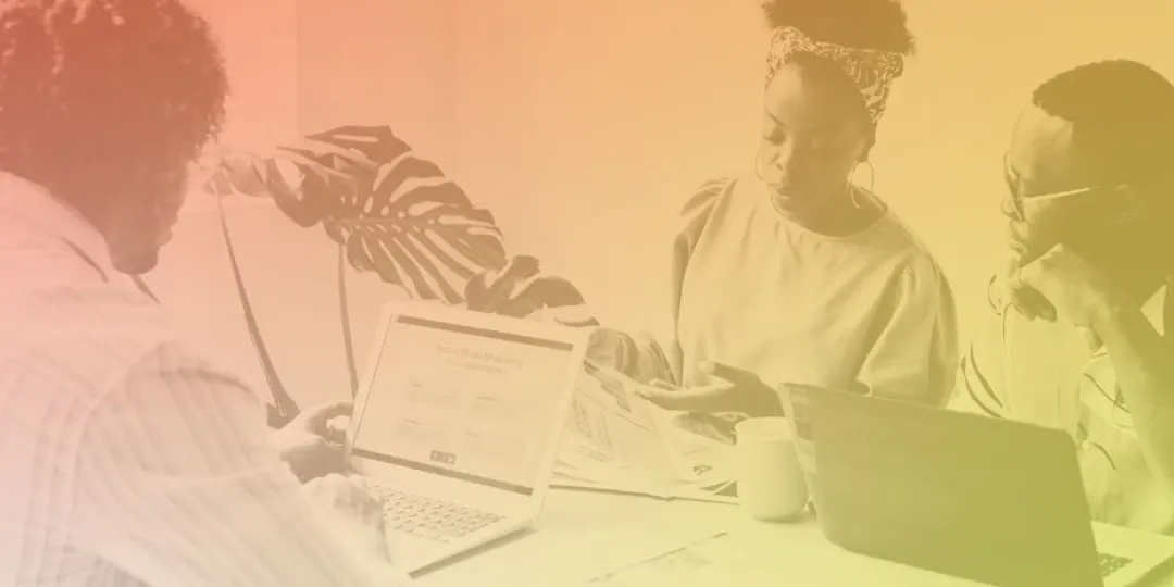 Image of three people in an office setting with laptops in front of them.